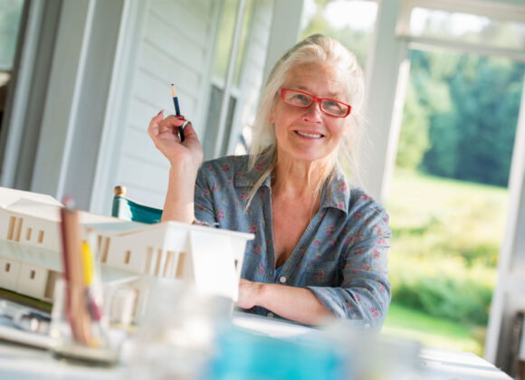 Willkommen Friends,USA,A farmhouse kitchen. A model of a house on the table. Designing a house. A woman sitting holding a pen.