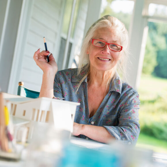 Friends,USA,A farmhouse kitchen. A model of a house on the table. Designing a house. A woman sitting holding a pen.