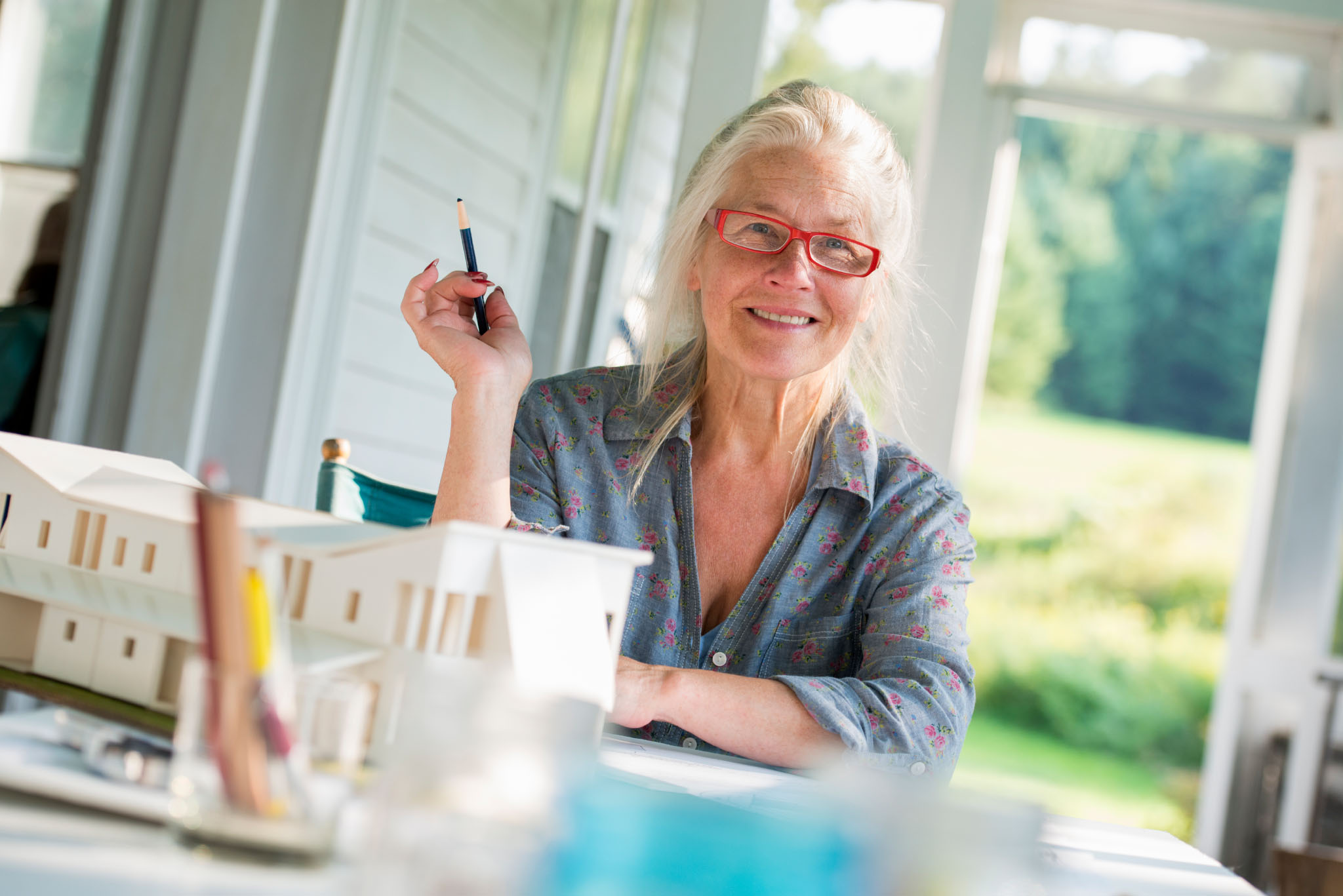 Friends,USA,A farmhouse kitchen. A model of a house on the table. Designing a house. A woman sitting holding a pen.